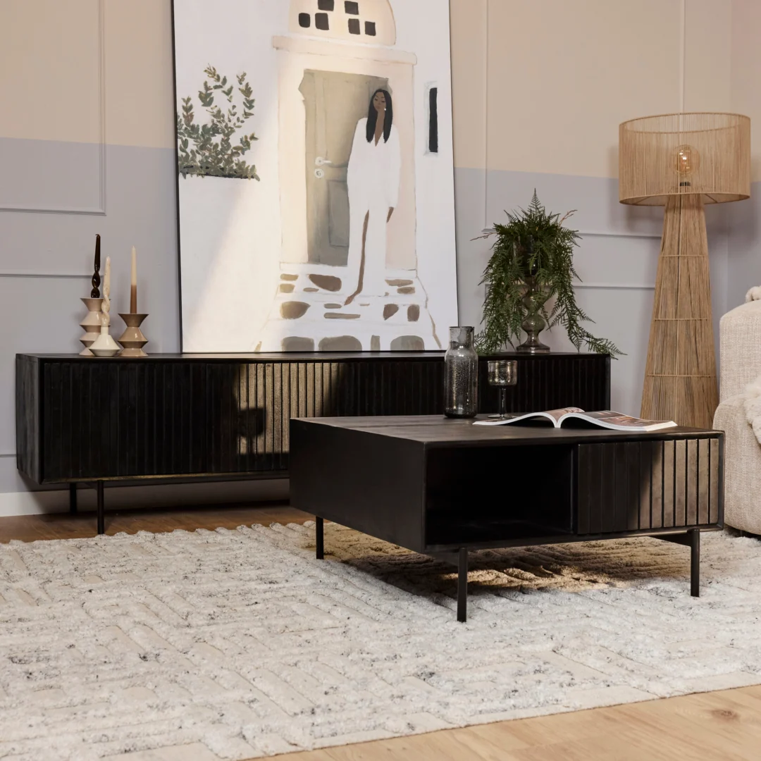 Een moderne woonkamer met een vloerkleed met structuur, een Salontafel 80 x 80 CM Vierkant Opbergvak als zwarte salontafel, zwart dressoir, hoge staande lamp, potplant en een groot schilderij van een vrouw in een deuropening dat op het dressoir rust.