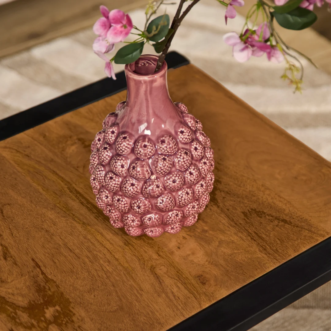 Op de bijzettafel Boaz 60 cm, met een houten oppervlak en een zwart metalen frame, staat een roze glazen vaas met structuurmotieven die roze bloemen vasthoudt.