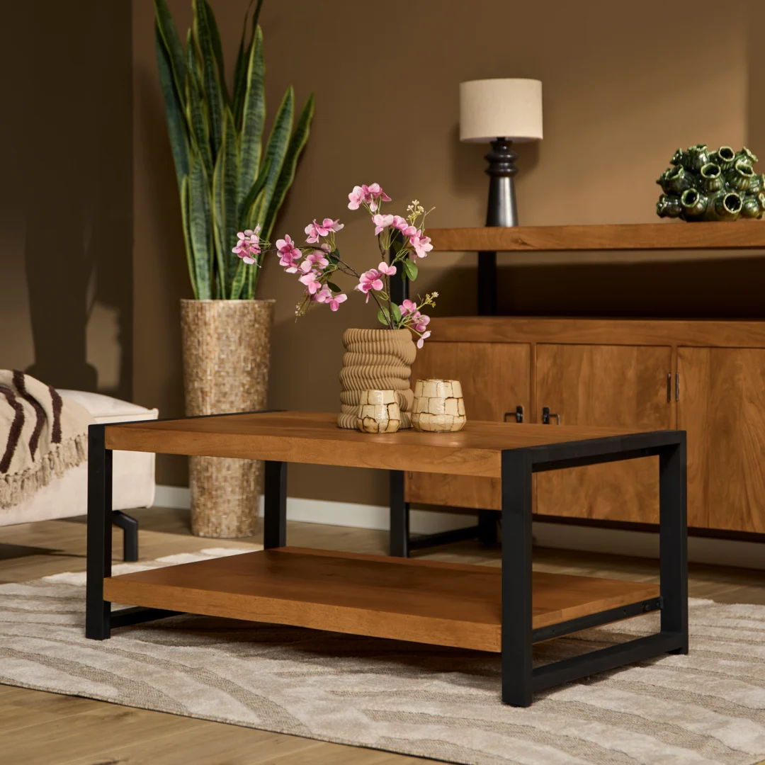Een moderne woonkamer met de Salontafel 110 x 60 CM, een houten salontafel met zwart metalen poten, met daarop een vaas met roze bloemen. Een grote plant in pot, houten dressoir, lamp en vloerkleed met patroon maken de gezellige ruimte compleet.