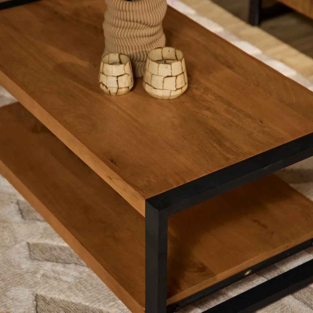 Een close-up van de Salontafel 110 x 60 CM, een houten salontafel met een zwart metalen frame, gedecoreerd met twee crèmekleurige kopjes en een vaas met structuur, geplaatst op een licht gedessineerd tapijt.