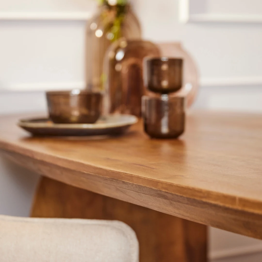 Een close-up van de Eettafel Tense 240 cm, met bruin glaswerk-kopjes, een schaal en een bord-vaas op de achtergrond en een beige stoel op de voorgrond.