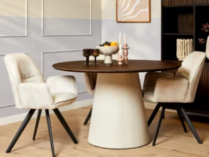 Elegante Madison eettafel met ronde houten blad en crèmekleurige voet. Beige stoelen met zwarte poten op een houten vloer. Sfeervolle belichting.