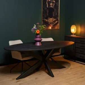 De Eettafel New York | Ovaal | 240 cm, een zwarte ovale eettafel, staat tussen twee beige stoelen in een moderne kamer met donkergroene muren, een houten vloer, kunstwerken en een kleine lamp boven op een kastje.