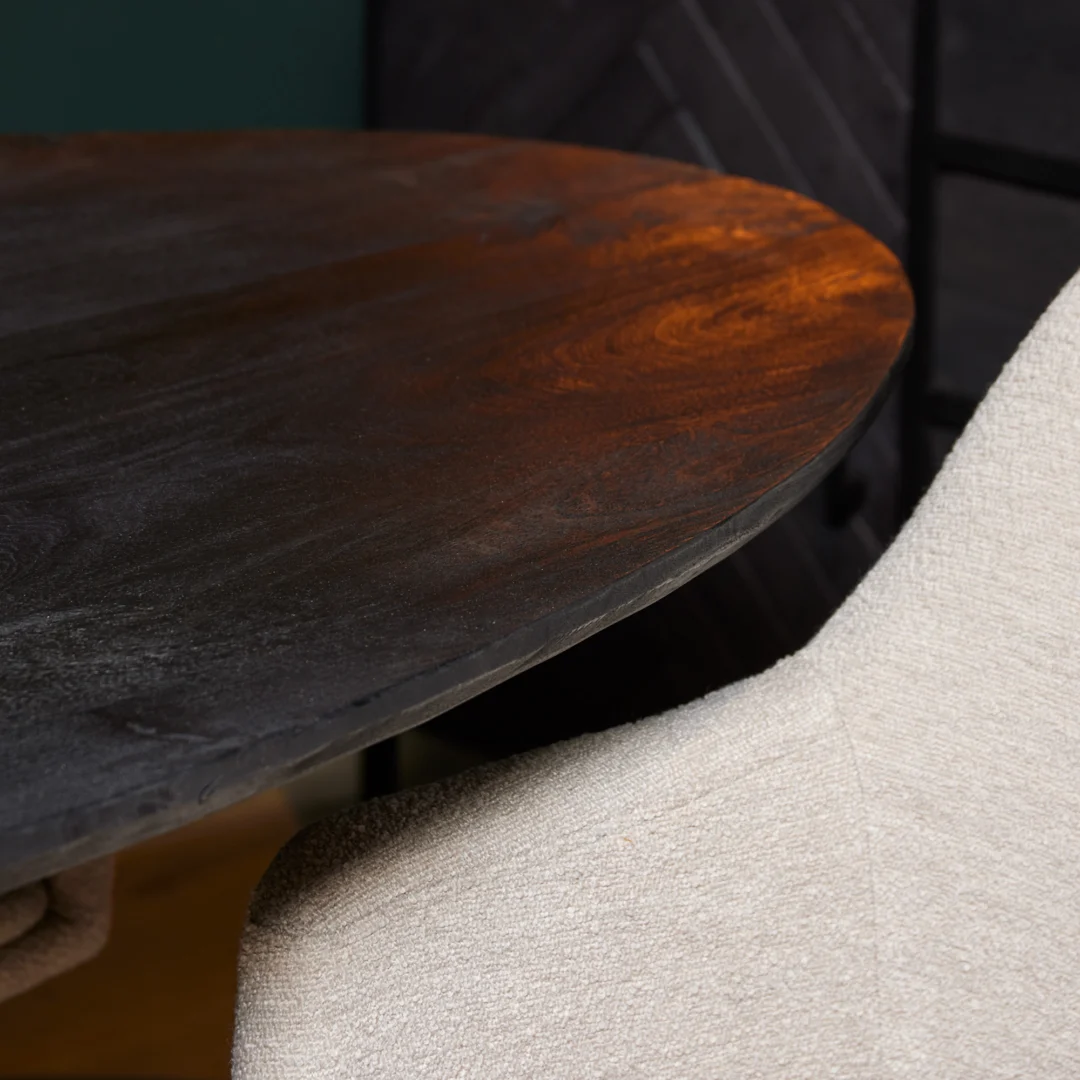 Close-up van de Eettafel New York | Ovaal | 180 cm, een ovale tafel van donker hout met een gladde afwerking, gecombineerd met een lichtbeige gestoffeerde stoel. Warme verlichting benadrukt het elegante tafeloppervlak.