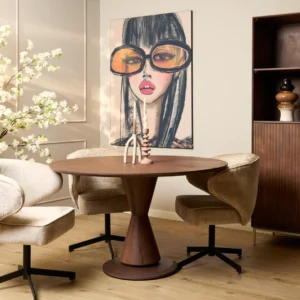 Een moderne eethoek is voorzien van de Eettafel Lima Walnoot 150 cm ronde tafel, drie beige draaistoelen, een sculpturaal middenstuk, bloesemtakken voor een natuurlijke touch en een groot schilderij van een vrouw met te grote glazen.