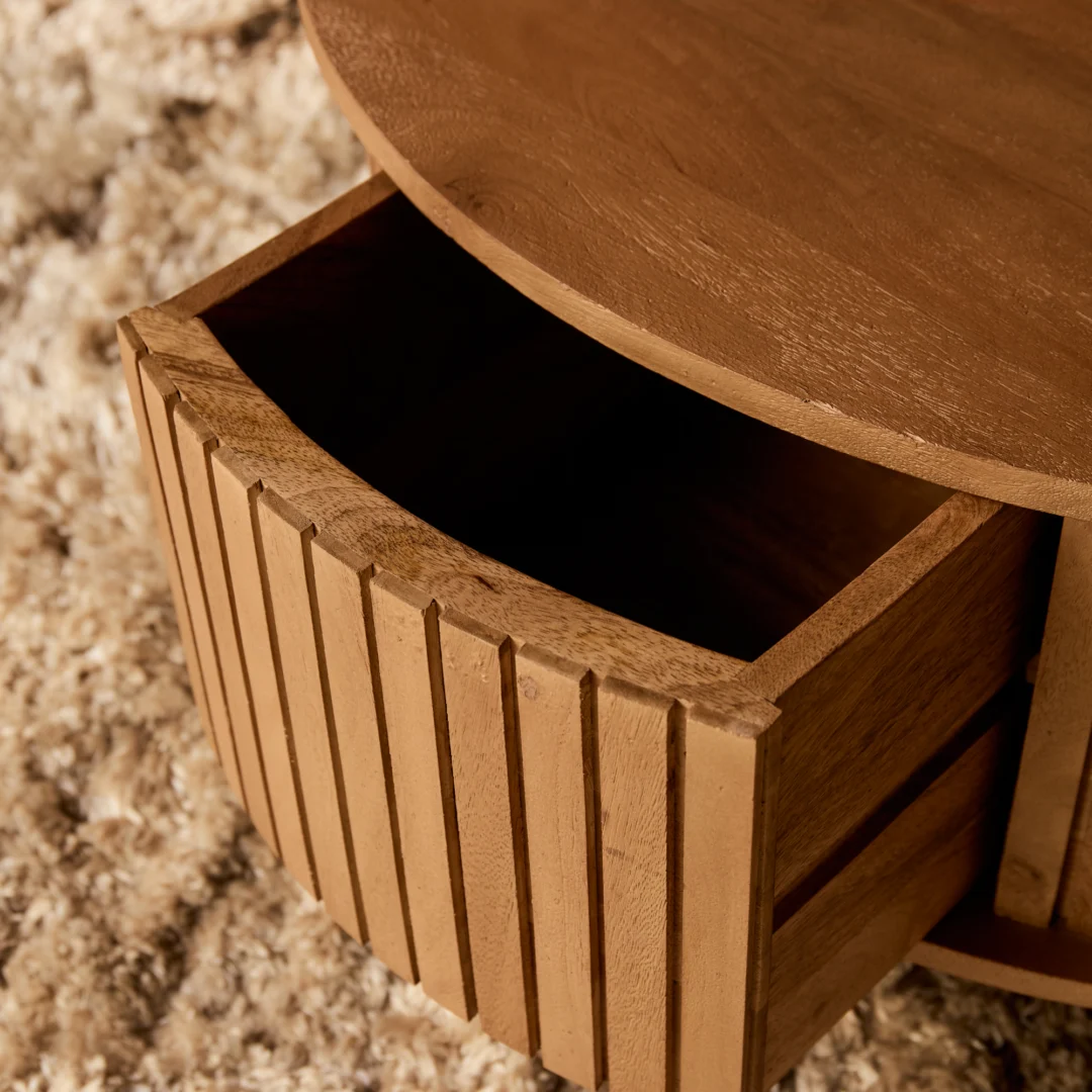Detailopname van een ronde salontafel met open lade. Houten materiaal met verticale latten. Zachte belichting, warme tinten.