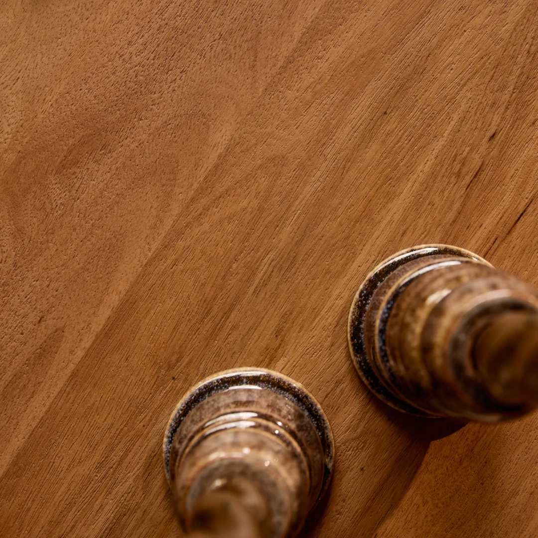 Bovenaanzicht van een houten salontafel met twee decoratieve objecten. Warm licht accentueert de houtnerf en de objecten. Tijdloos design.