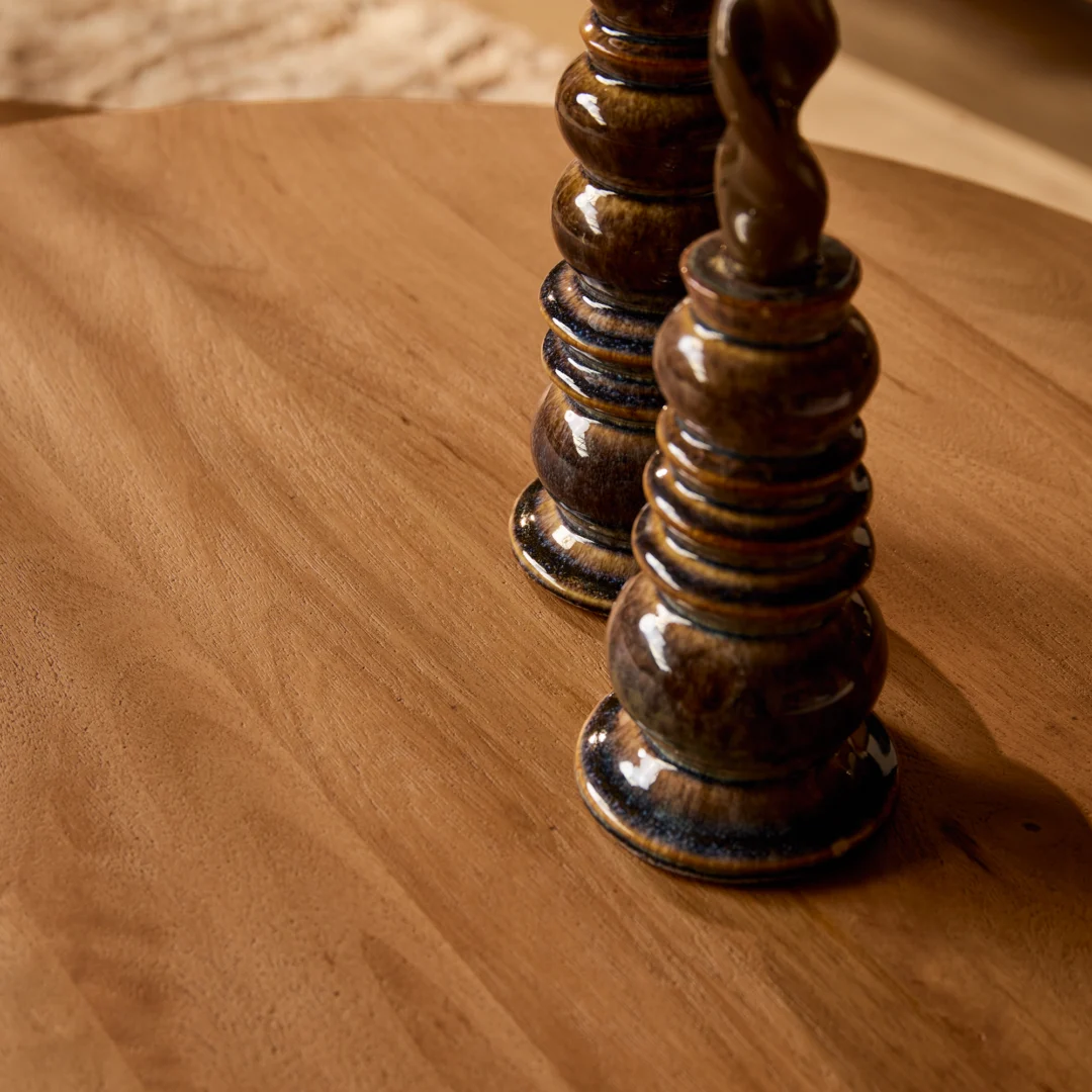 Twee bruine, gedraaide kandelaars op een houten salontafel. Warm licht accentueert het houtnerf en het glazuur. Tijdloos design.