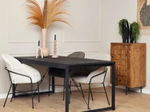 Een moderne eethoek met de Eettafel Boaz Zwart (140 cm), drie stoelen met kussens, decoratieve vazen met gedroogde grassen, een houten kast en een lichthouten vloer tegen beige wanden met panelen.