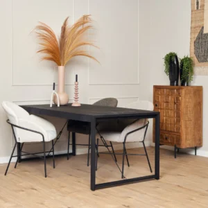 Een moderne eethoek met de Eettafel Boaz Zwart (140 cm), drie stoelen met kussens, decoratieve vazen met gedroogde grassen, een houten kast en een lichthouten vloer tegen beige wanden met panelen.