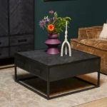 De Salontafel 80 x 80 CM Vierkant Compact met laden staat op een beige vloerkleed, met daarop een paarse vaas met gemengde bloemen en een moderne witte kandelaar. Op de achtergrond staan een bruine ribfluwelen bank en een donkere kast.