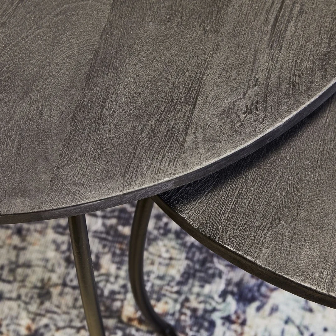Close-up van twee overlappende Salontafel Zwart 70 x 40 CM Rond tafels met donkergrijze textuur en dunne metalen poten, op een tapijt met veelkleurig patroon.