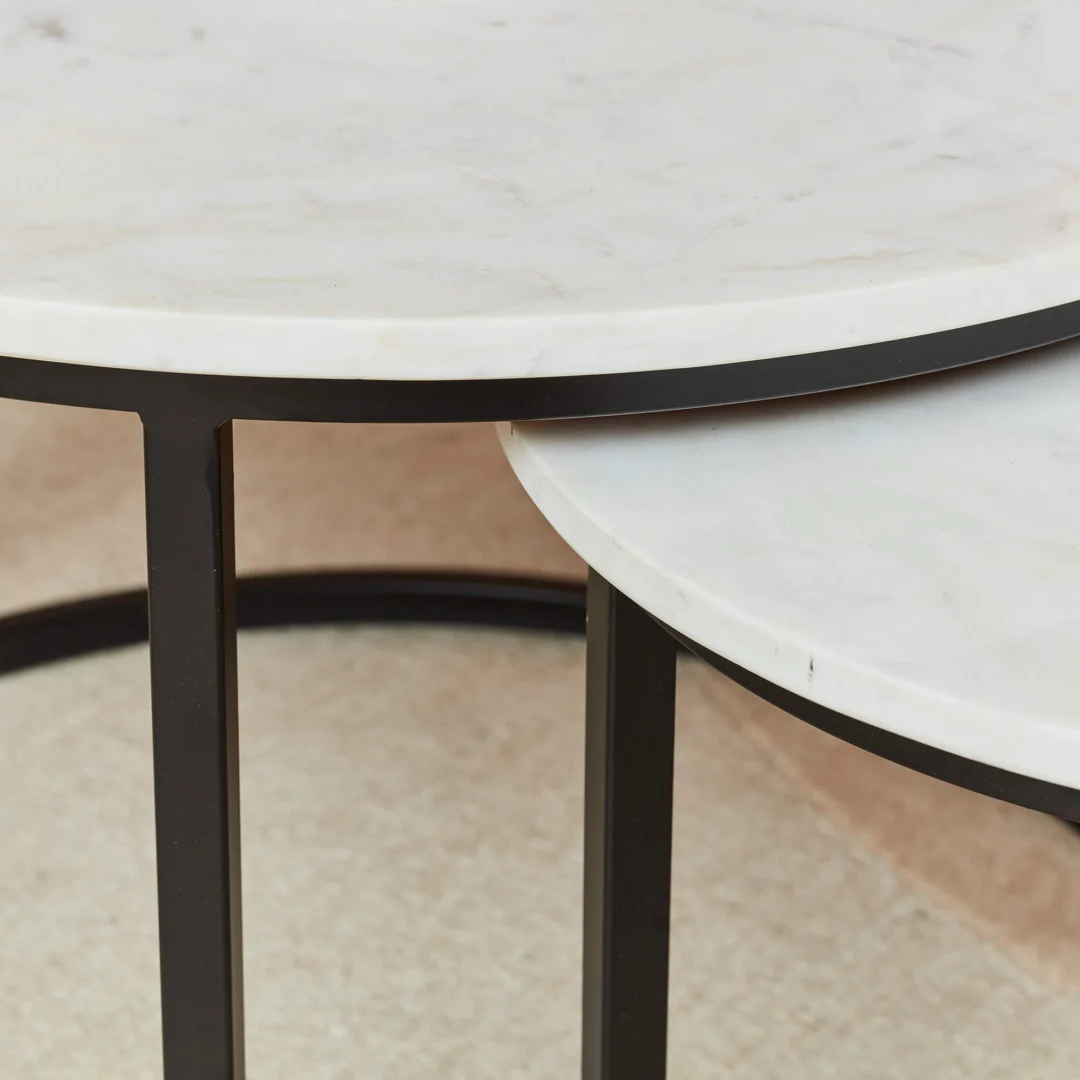Twee Salontafels Wit 70 x 50 CM Rond Marmer met wit marmeren bladen en zwart metalen poten zijn gedeeltelijk in elkaar geschoven op een lichtgekleurd oppervlak.