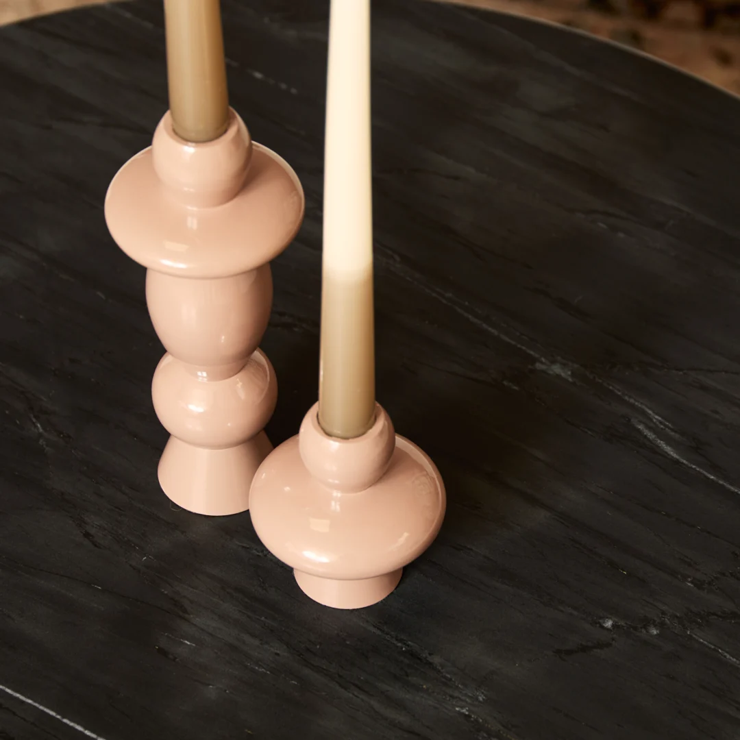 Twee beige kaarsen in glanzende, gebeeldhouwde kaarsenhouders staan op Salontafel Zwart 70 x 70 CM Rond Marmer, een donkere ronde marmeren tafel.