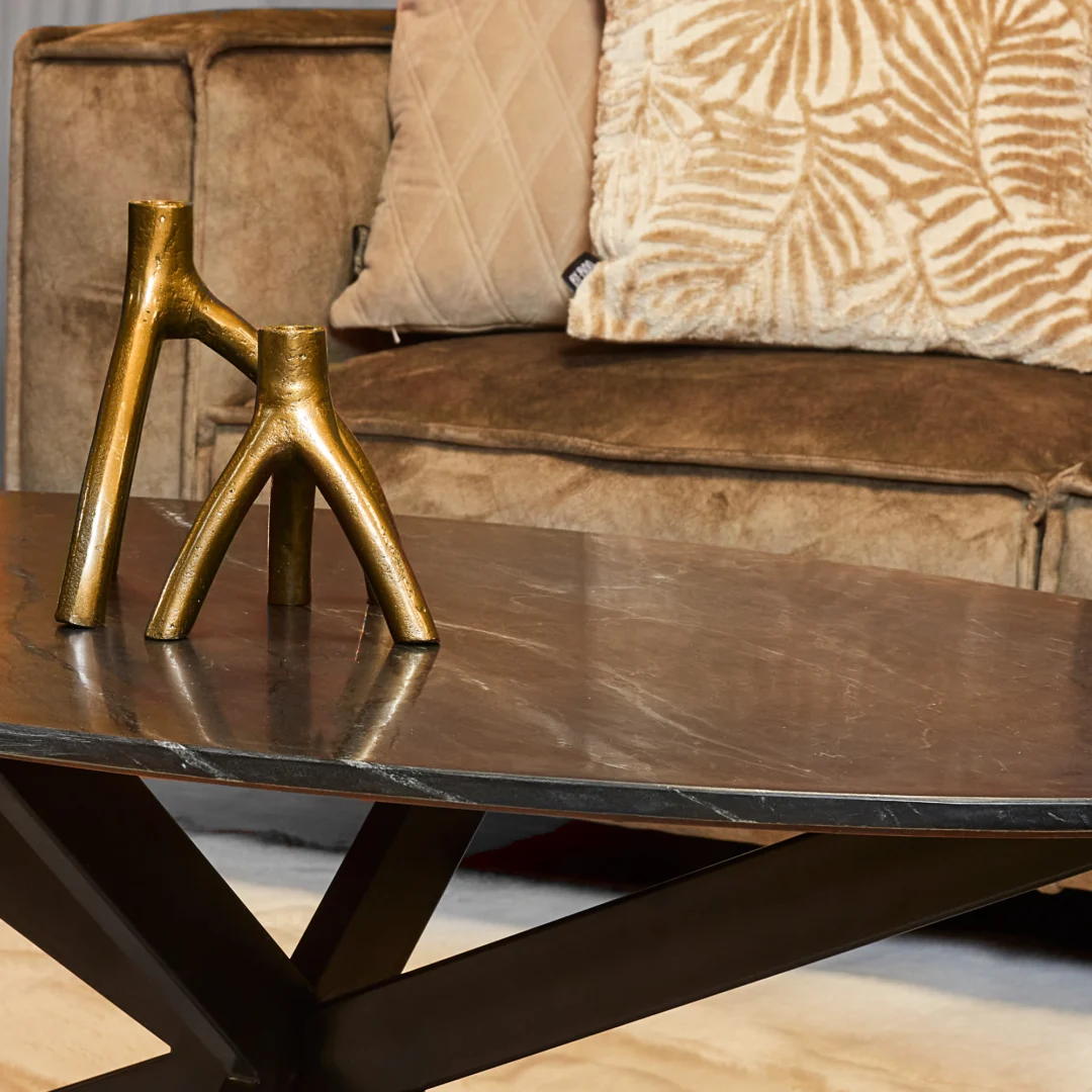 Een moderne woonkamer met een bruin fluwelen bank, beige kussens met patroon en een Salontafel Zwart 130 CM Ovaal Marmer met daarop een gouden decoratieve sculptuur.