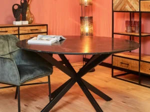 Een moderne eethoek met de Eettafel Lynn, een ronde zwart marmeren tafel (130 cm), een groen fluwelen stoel, een open boek, houten dressoirs met decor, een verlichte vloerlamp en een roze muur op de achtergrond.