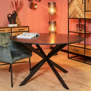 In een moderne eetkamer staat de Eettafel Lynn, een ronde tafel van zwart marmer (150 cm), gecombineerd met een stoel van groen fluweel, een houten kast en een decor. Warme verlichting en roze muren versterken de gezellige, stijlvolle sfeer. Een open boek rust op de tafel.