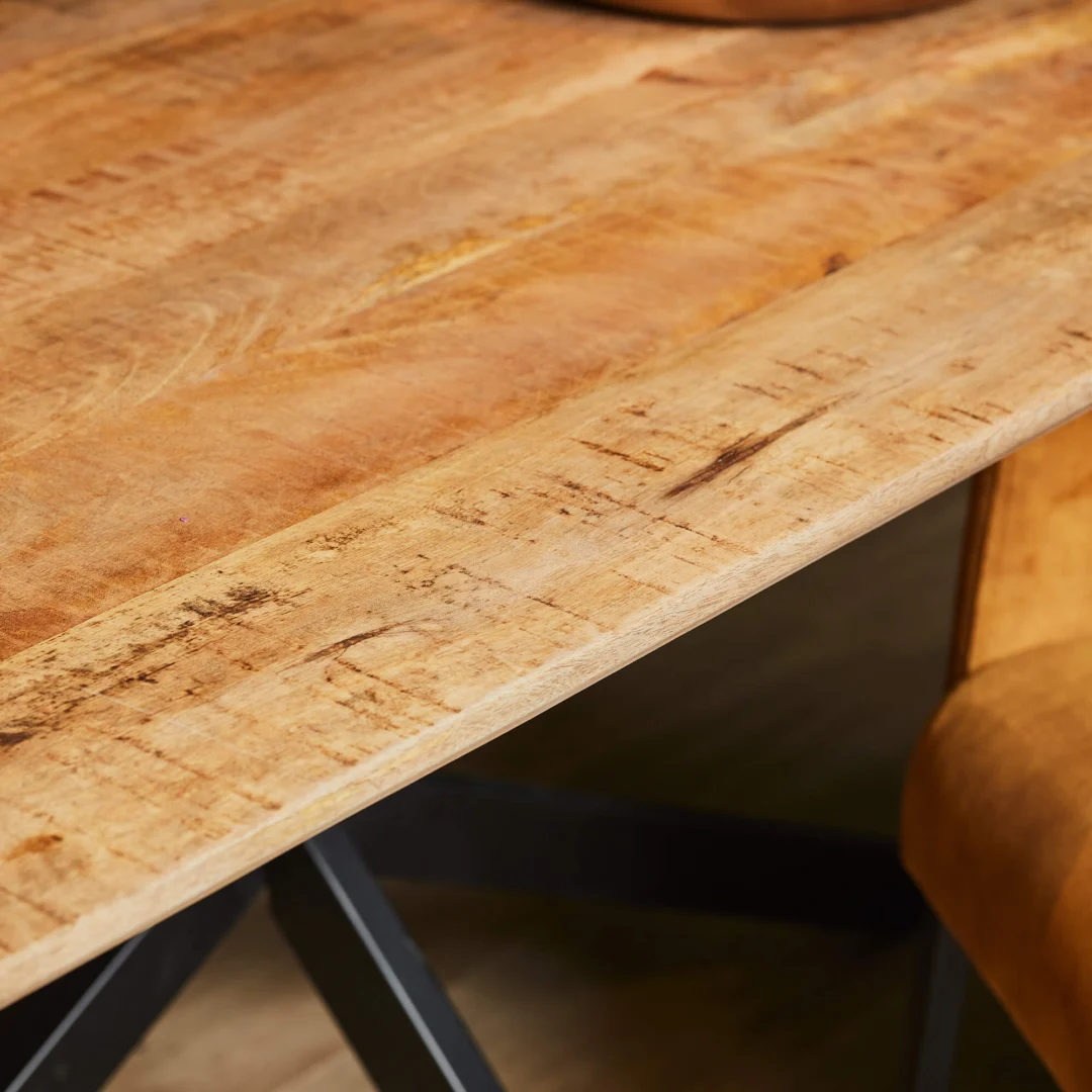 Detailopname van een houten eettafel Arlington met een metalen onderstel. Het hout is lichtbruin en heeft een warme uitstraling.
