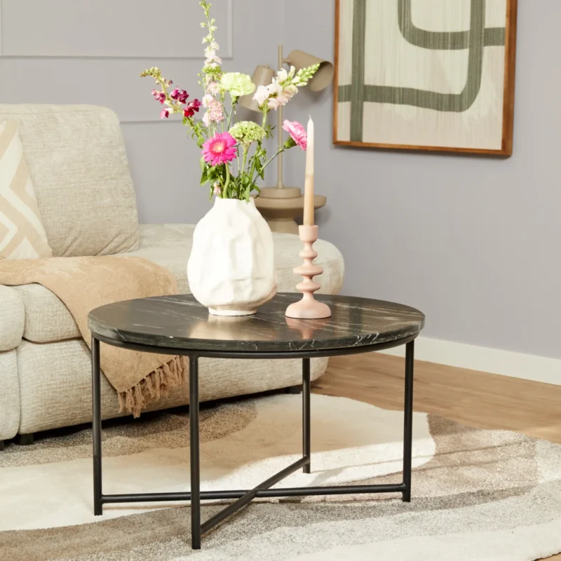 Een moderne woonkamer met de Salontafel Zwart 75 x 75 CM Vierkant Marmer salontafel met een witte vaas bloemen en een roze kandelaar, naast een beige bank met een bruine plaid en een groot abstract schilderij aan de muur.