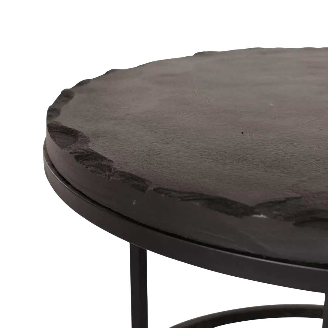 Een close-up van de Salontafel Zwart 61 x 61 CM Steen toont het ronde zwarte blad met een ruwe, steenachtige rand en slanke metalen poten, die de tafel een natuurlijke uitstraling geven.