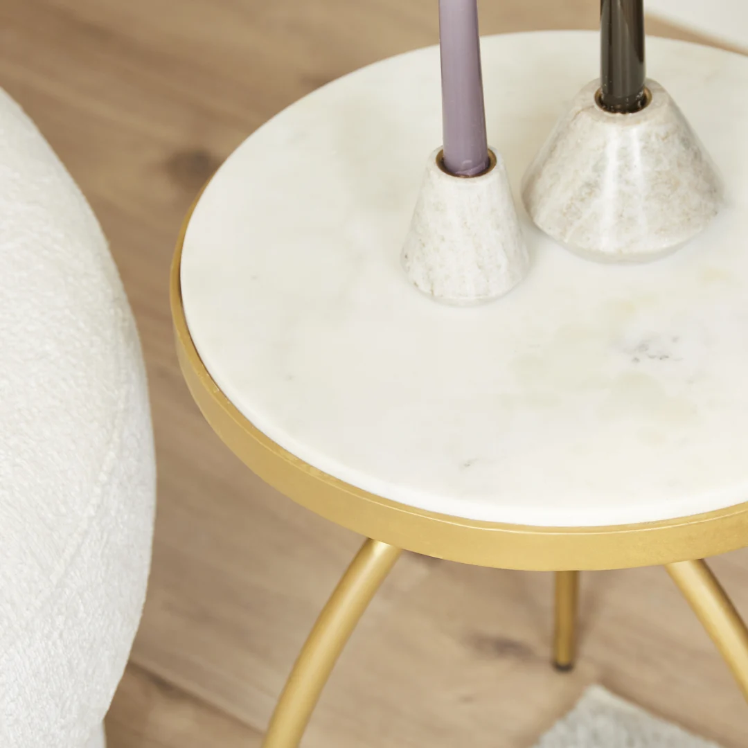 De bijzettafel Kay | Wit marmer 40 cm toont twee marmeren kandelaars met hoge kaarsen. Een deel van een stoel met witte textuur en een houten vloer zijn ook zichtbaar.