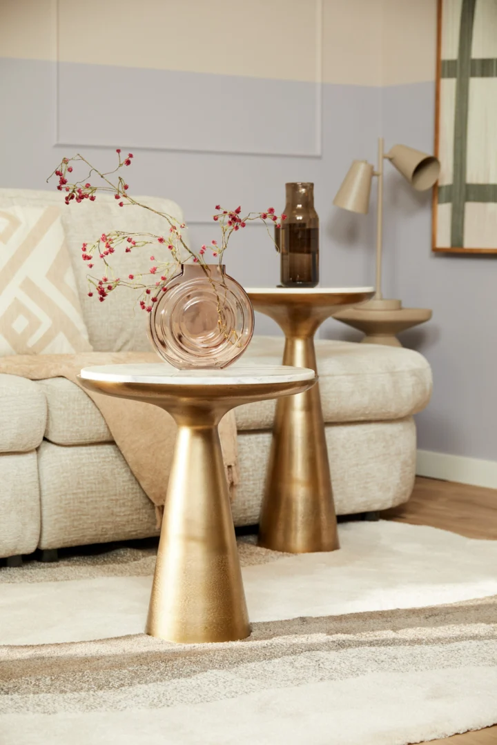 In een moderne woonkamer staan twee Bijzettafel Essy Large tafels met een 45 cm wit marmeren blad - op de ene staat een glazen vaas met rode bessen, op de andere een bruine glazen fles - voor een beige bank met een neutrale inrichting.