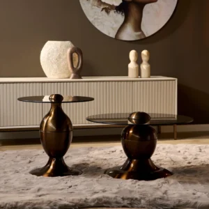 Een paar Salontafel Industrieel bronzen bijzettafeltjes met ronde glazen bladen staan op een beige vloerkleed voor een wit dressoir, geaccentueerd door vazen en gedeeltelijke portretkunst op de achtergrond.