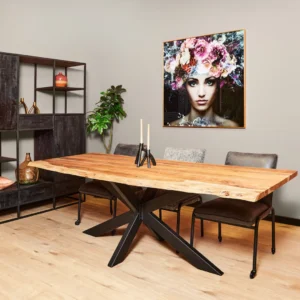 Een moderne eetkamer met de Boomstamtafel Live Edge 200 cm houten tafel met zwarte metalen poten, drie grijze stoelen, decoratieve planken, een bladplant en muurschilderingen van een vrouwengezicht met kleurrijke bloemen.