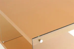 Een close-up van de Bijzettafel Goud Glas toont het moderne, minimalistische ontwerp met een lichtbruin glazen blad, helder glazen zijkanten en metalen hoekbevestigingen voor een strakke look.