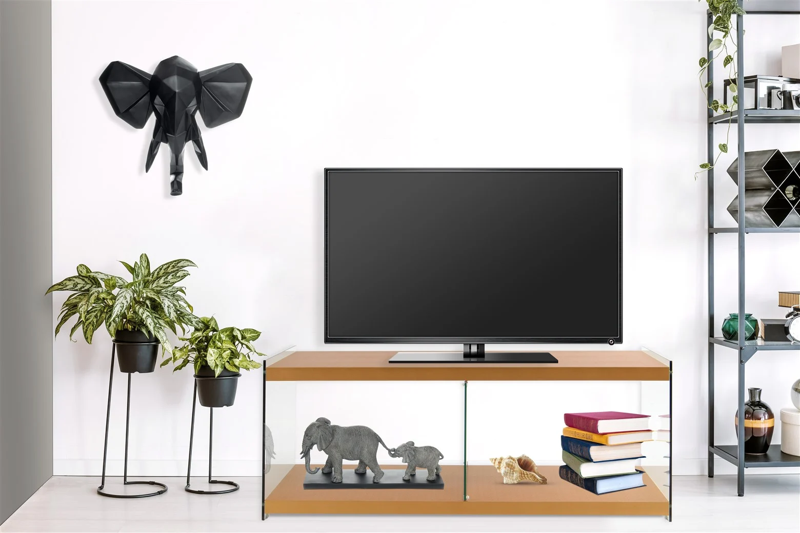 Een moderne woonkamer met een tv op de Bijzettafel Goud Glas, potplanten, boeken, olifantenbeeldjes en geometrische olifantenkunst op een witte muur. Aan de rechterkant staan versierde planken.