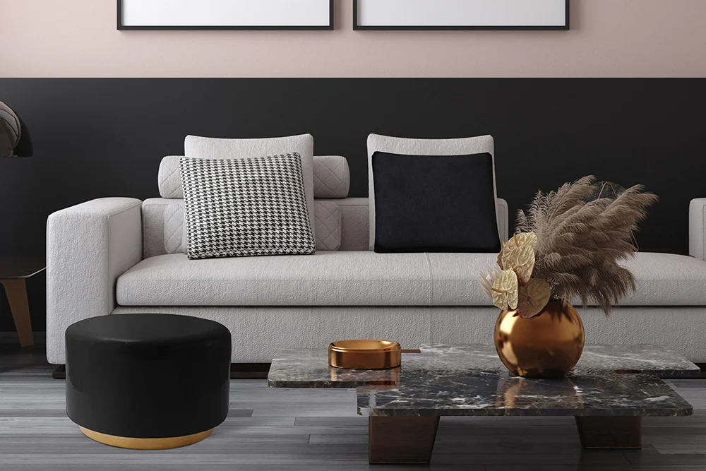 Een moderne woonkamer met een lichtgrijze bank, zwarte kussens met patronen, een Bijzettafel Zwart Rond Ijzer en een marmeren salontafel met een gouden vaas met gedroogde planten. De muur heeft zwarte en beige tinten.