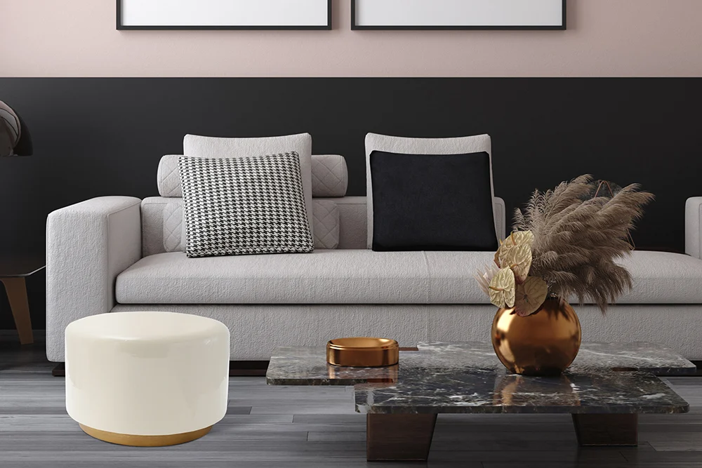Een moderne woonkamer met een lichtgrijze bank, zwarte en houndstooth kussens, een marmeren salontafel met gouden accenten, de Bijzettafel Ivoor Rond Ijzer Klassiek, een gouden vaas met gedroogd pampagras en een ronde witte poef.
