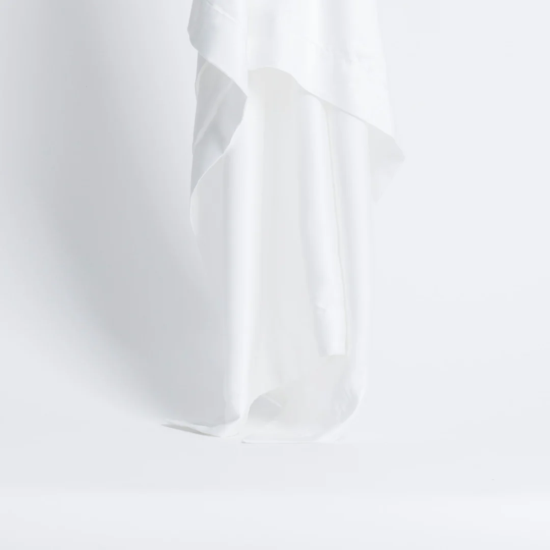 De Dekbedovertrek Wit 200x200, gemaakt van een wit, luchtig en vochtregulerend materiaal, valt sierlijk met zachte plooien tegen een egale achtergrond voor een minimalistische en frisse uitstraling.