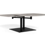 Grijze salontafel met een zwart metalen onderstel, gefotografeerd in een lichte studio. Het tafelblad heeft een betonlook en een afgeronde rechthoek vorm.