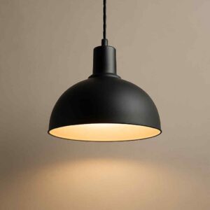 Zwarte hanglamp van metaal, hangend aan een zwart snoer. Warm, zacht licht schijnt naar beneden. Design lamp voor de woonkamer.