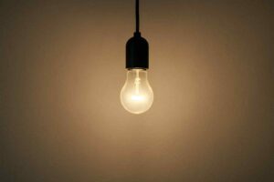 Een gloeilamp met zwart snoer en fitting tegen een beige achtergrond. Warm licht schijnt op de muur. Design voor jouw woonkamer.