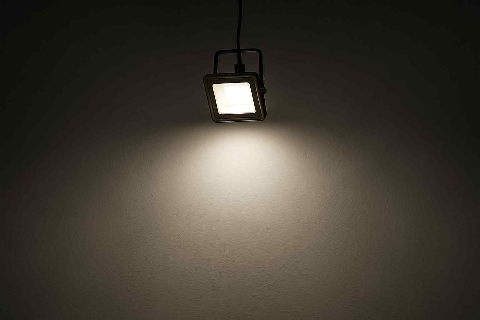 Een vierkante spot verlicht een donkere muur. Het licht is helder en wit. Het design is modern en minimalistisch. Comfortabele verlichting.