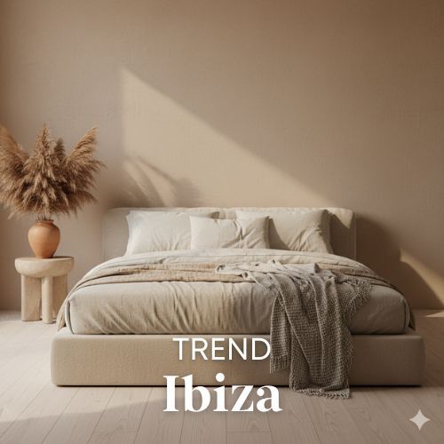 Beige slaapkamer met houten vloer en zachte belichting. Een bed met veel kussens en een plaid. Naast het bed staat een vaas met pampasgras.