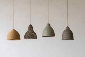 Vier hanglampen van gerecyclede materialen tegen een witte achtergrond. De lampen hebben verschillende vormen en texturen in bruin en grijs.