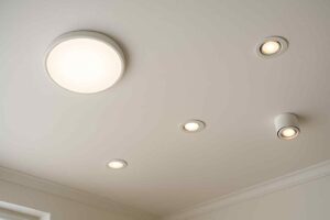 Wit plafond met ronde plafondlamp en inbouwspots. De lampen geven een warme gloed. Design verlichting voor een comfortabele woonkamer.