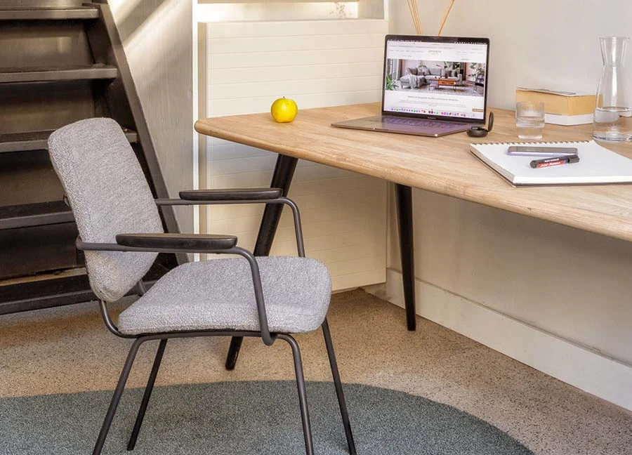 Strakke studeerkamer woonidee met houten bureau en grijze stoel. Laptop, notitieboek en appel op het bureau. Trap en lichte wand op de achtergrond.
