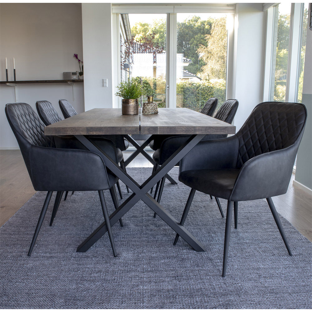 Zijaanzicht van zes Harbo eetkamerstoelen in donkergrijs PU met zwarte poten rondom een houten tafel, geplaatst op een grijs vloerkleed.