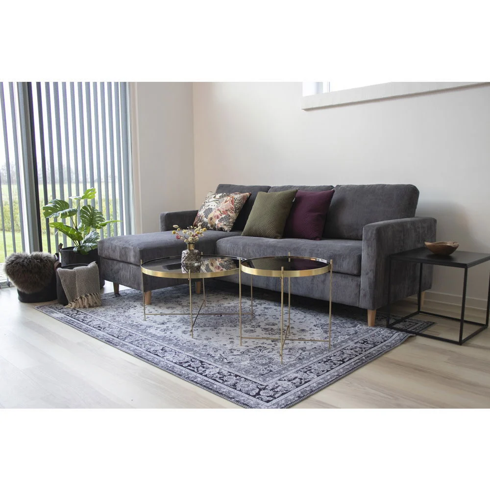 Living room scene showcasing a zwart square bijzettafel with a metal frame, next to a grey corner sofa on a patterned rug, vanuit een schuin perspectief.
