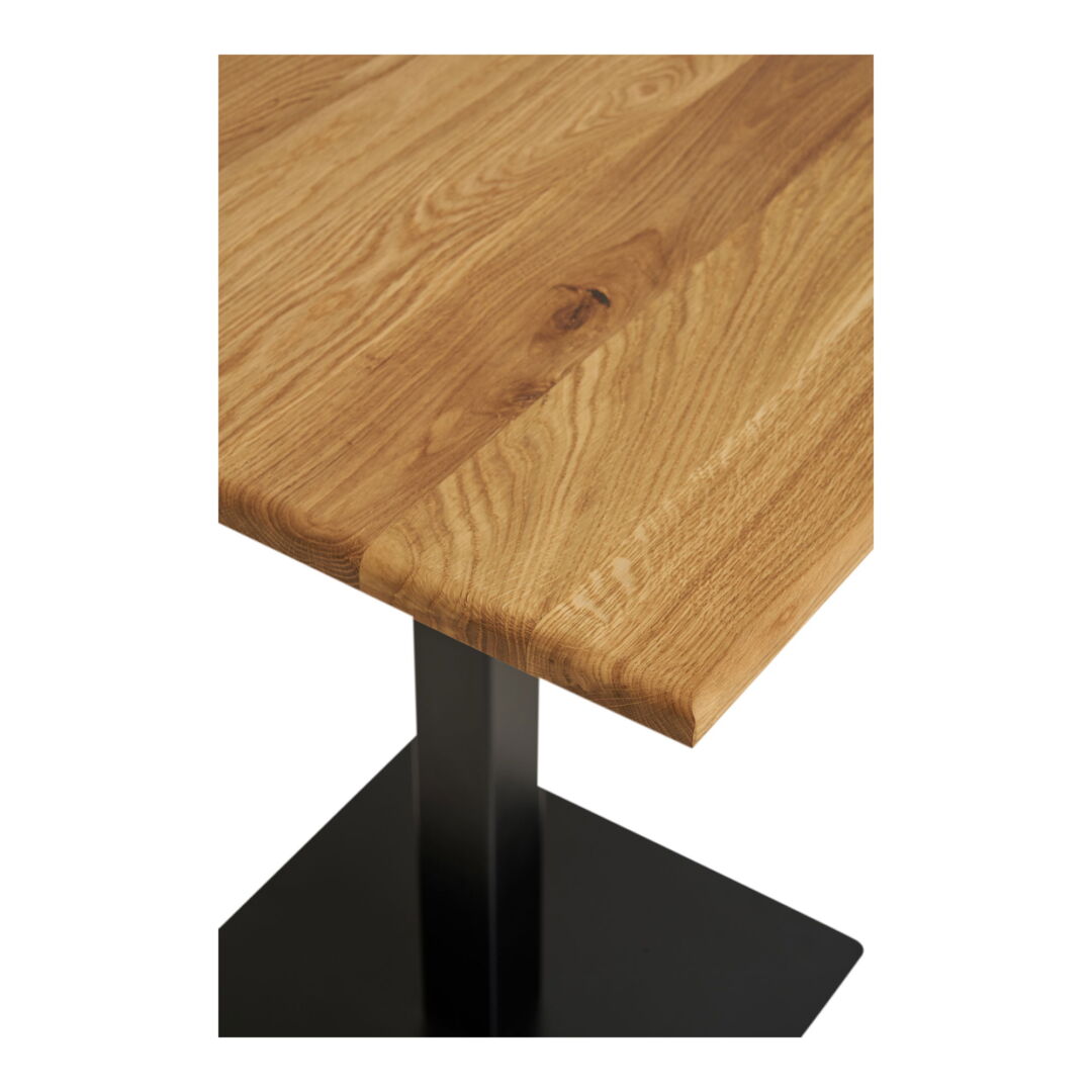 Close-up of a Lignano eettafel, showcasing the vierkant wooden top with visible wood grain and a black metal base set against a white achtergrond.