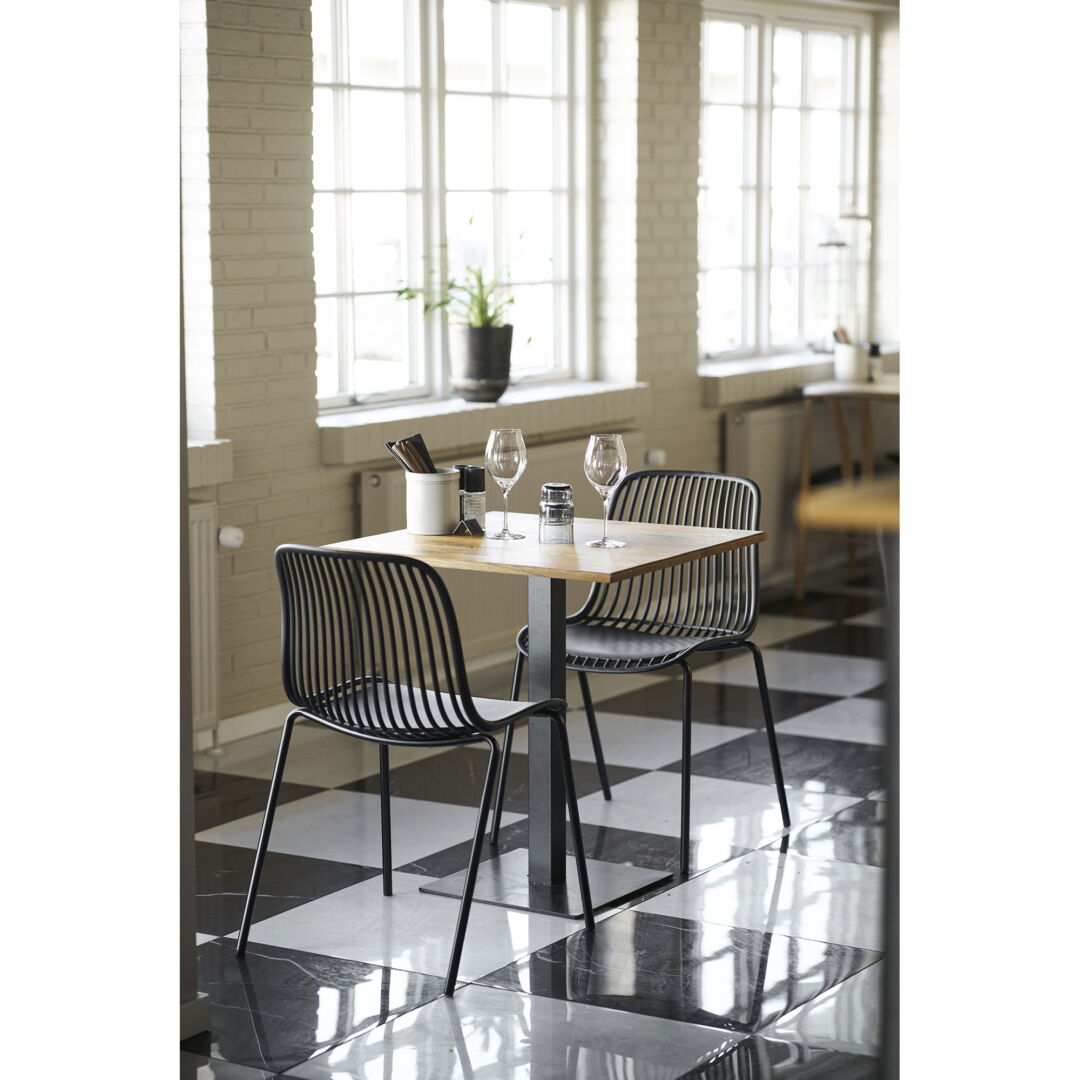 Eettafel Lignano vierkant, houten blad, zwarte metalen poten, met twee stoelen, wijnglazen en bestekhouder, hoge hoek, heldere verlichting.