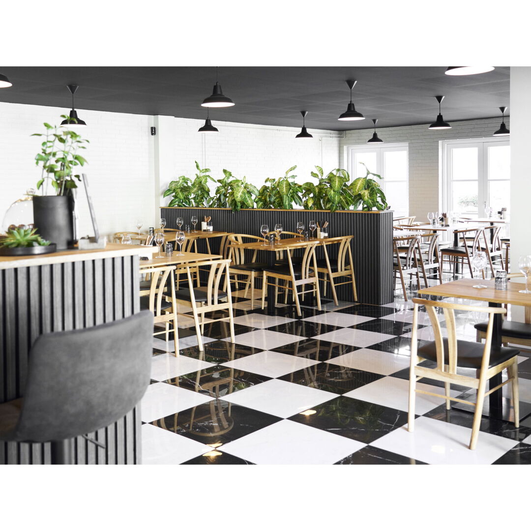 Interior shot of a restaurant featuring square Eettafel sets, black and white checkered floor, and a modern design with veel lichtinval van buiten.