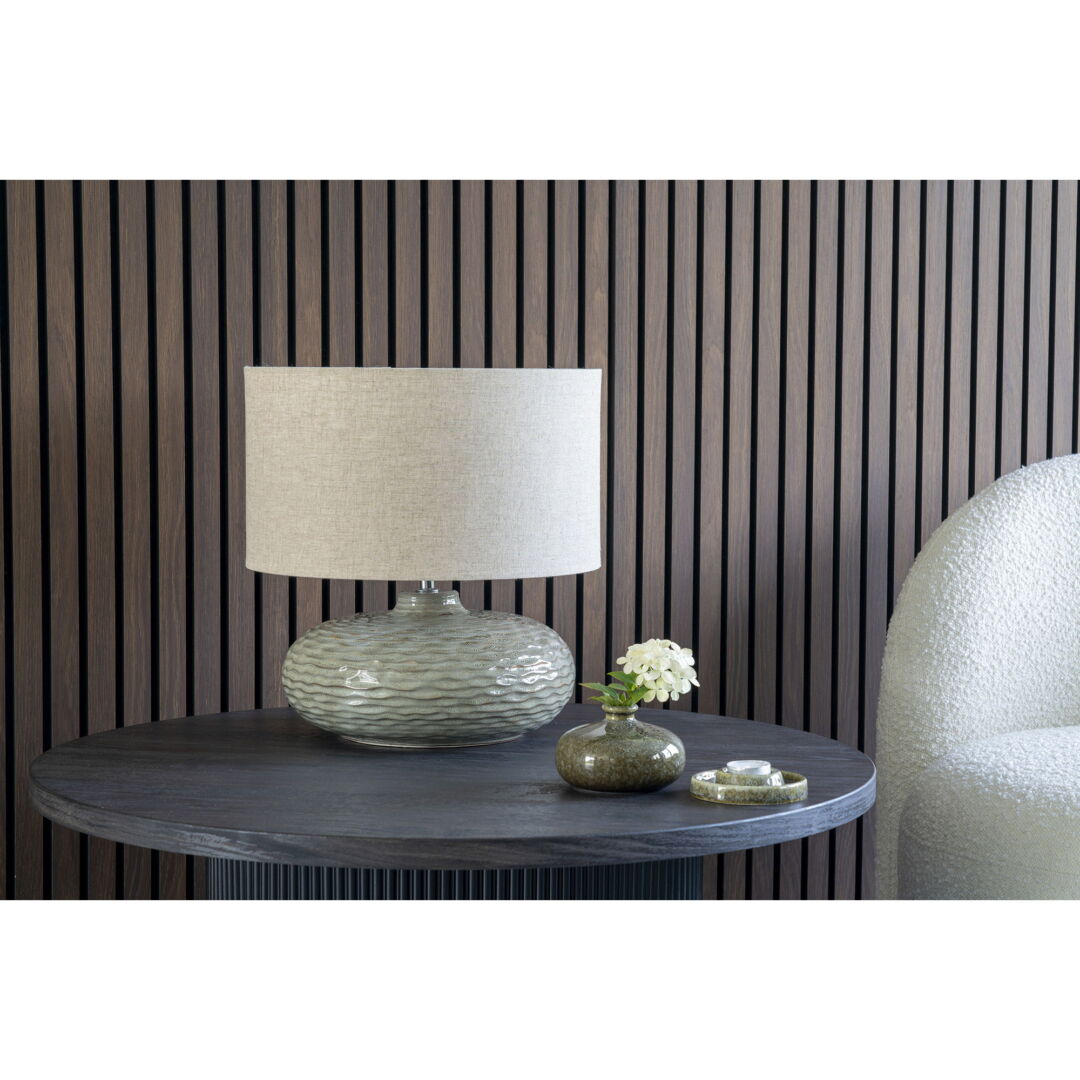 Close-up of a round design salontafel with a textured lamp, a small vase with a flower, and dark houten achtergrond. Warm, neutrale kleuren.