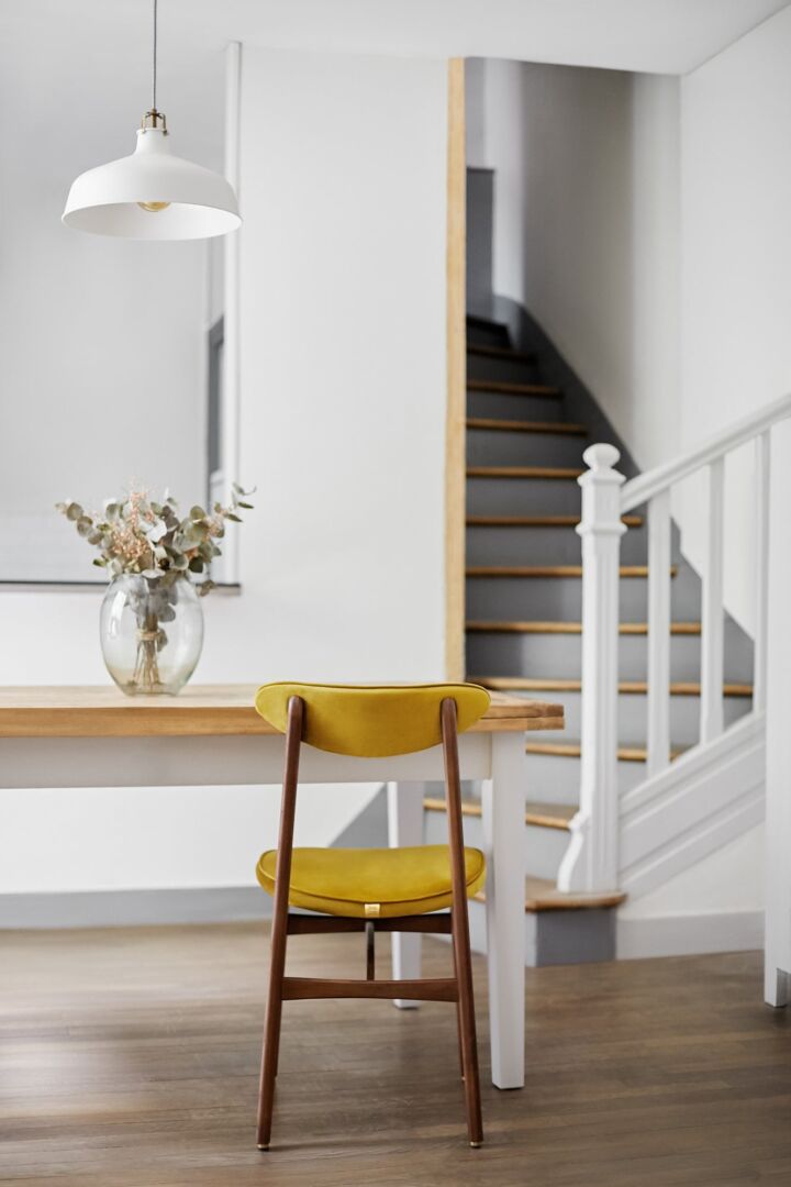 Eetkamerstoel 200-190 Fluweel Schildpad Met Naturel Hout: Gele fluwelen stoel met houten frame aan een houten tafel.