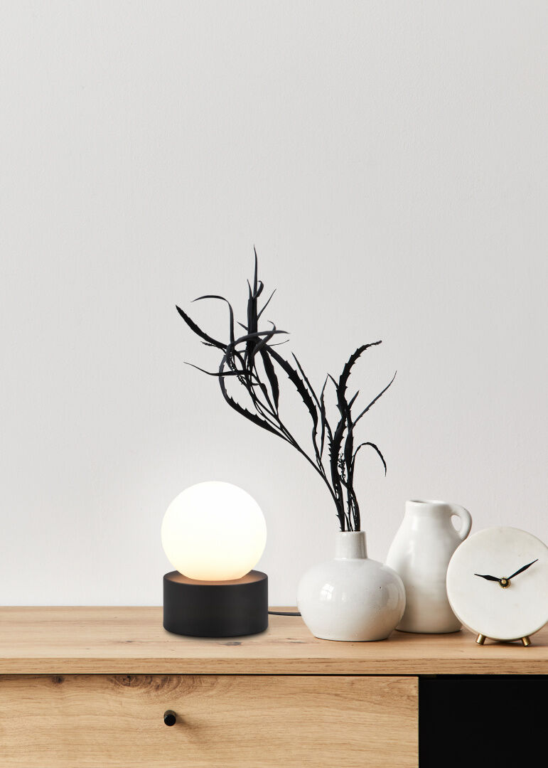 REALITY Tafellamp COUNTESS: Moderne tafellamp met bolvormige lampenkap op een houten voet, naast decoratieve vaas en klok.