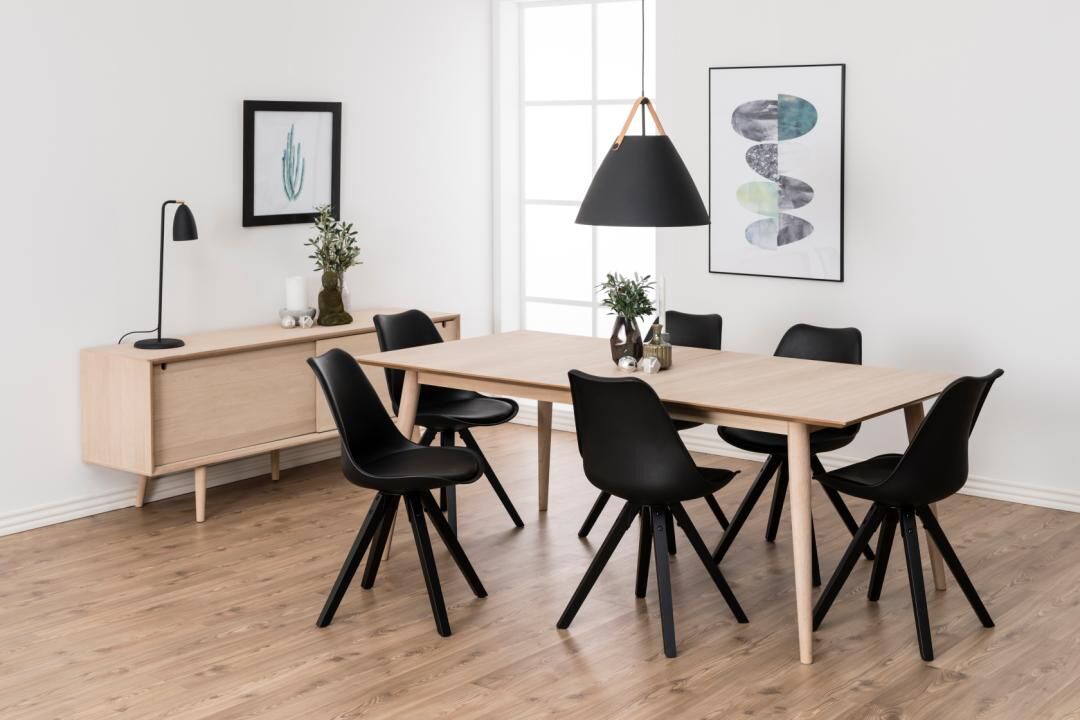 Eetkamer met lichte houten tafel, zes zwarte Dima eetkamerstoelen, en een lichte houten dressoir.